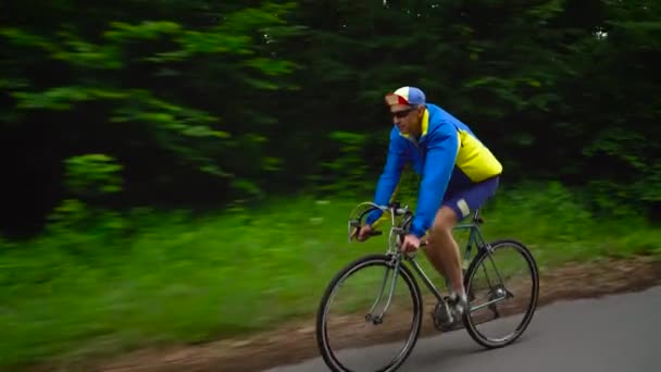 Middle-aged man is riding a road bike along a forest road, slow motion - Footage, Video