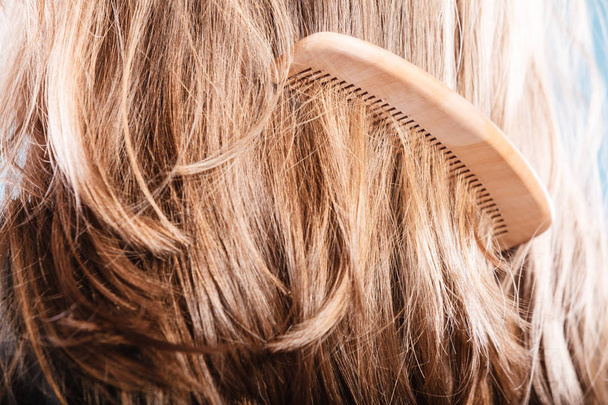 Ίσια καστανά μαλλιά με ξύλινη χτένα κινηματογράφηση σε πρώτο πλάνο - Φωτογραφία, εικόνα