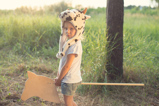 Дитина в смішному капелюсі тварин грає з дерев'яним іграшковим конем
 - Фото, зображення