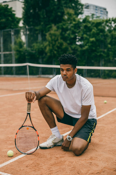 Young man hanging out in the tennis courts sitting on ground. - Foto, afbeelding