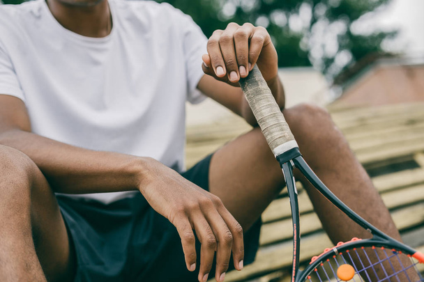 Close-up of a tennis player holding a racket sitting on a bench - Фото, зображення