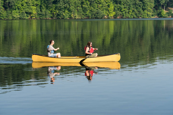 Couple pagayant en canot jaune sur un lac bordé d'arbres
 - Photo, image