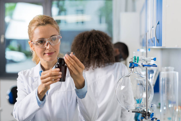 Female Scientific Researcher In Laboratory Doing Research, Woman Working With Chemicals Over Group Of Scientist - Valokuva, kuva