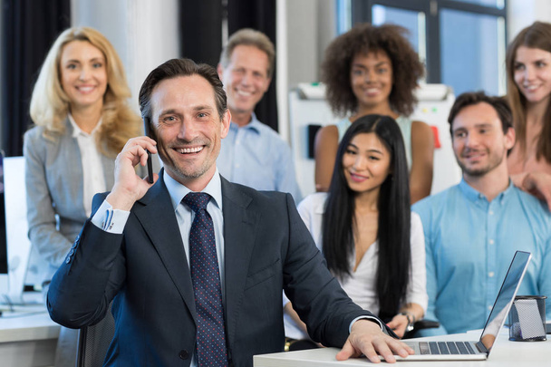 Επιχειρηματίας αφεντικό μιλάει στο κινητό τηλέφωνο κλήση από μίγμα αγώνα επαγγελματίες άνθρωποι ομάδα στέκεται πίσω στο σύγχρονο γραφείο, επιχειρηματίες ευτυχής χαμογελαστοί ομάδα - Φωτογραφία, εικόνα