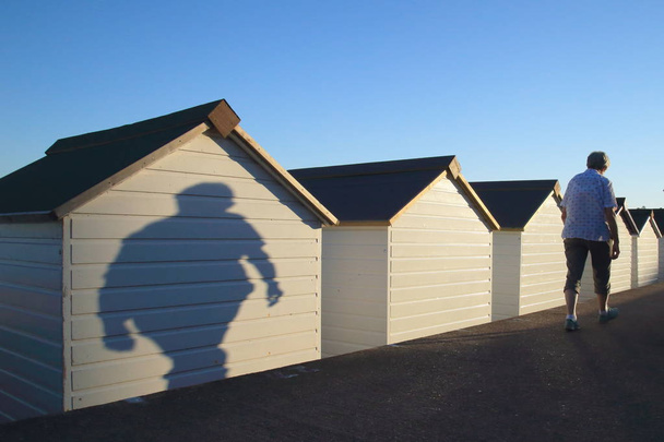 Sombras de pessoas passando por cabanas de praia
 - Foto, Imagem
