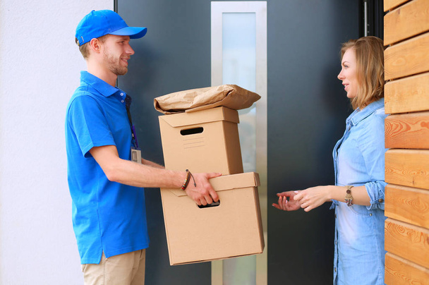 Smiling delivery man in blue uniform delivering parcel box to recipient - courier service concept - Φωτογραφία, εικόνα