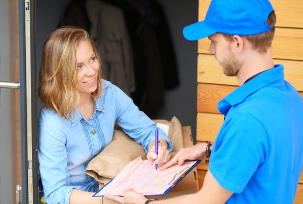Smiling delivery man in blue uniform delivering parcel box to recipient - courier service concept - Foto, imagen