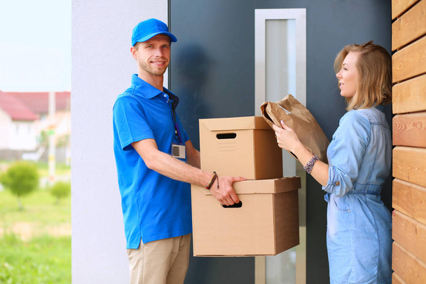 Smiling delivery man in blue uniform delivering parcel box to recipient - courier service concept - Photo, Image
