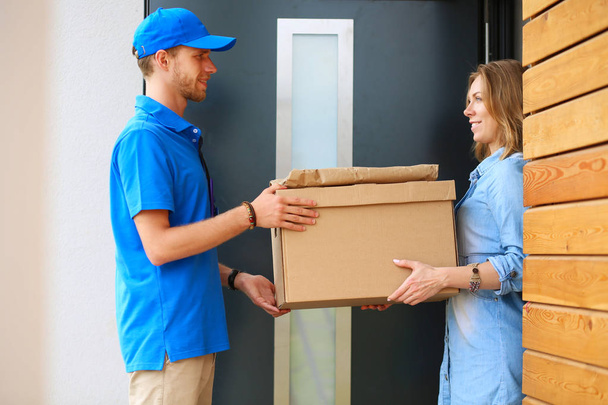 Smiling delivery man in blue uniform delivering parcel box to recipient - courier service concept - Foto, afbeelding