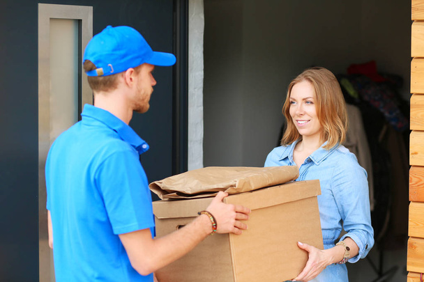 Smiling delivery man in blue uniform delivering parcel box to recipient - courier service concept - Photo, image