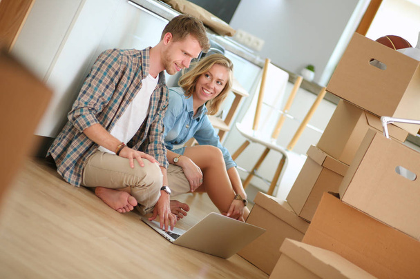 Young couple moving in new home.Sitting on floor and relaxing after unpacking.Looking something on laptop - Fotoğraf, Görsel
