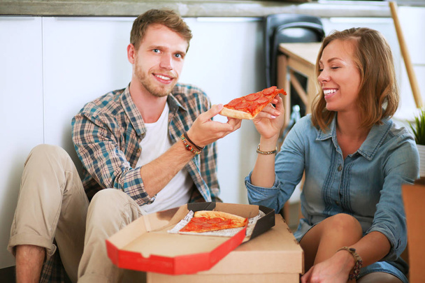 Young couple have a pizza lunch break on the floor after moving into a new home with boxes around them - Valokuva, kuva