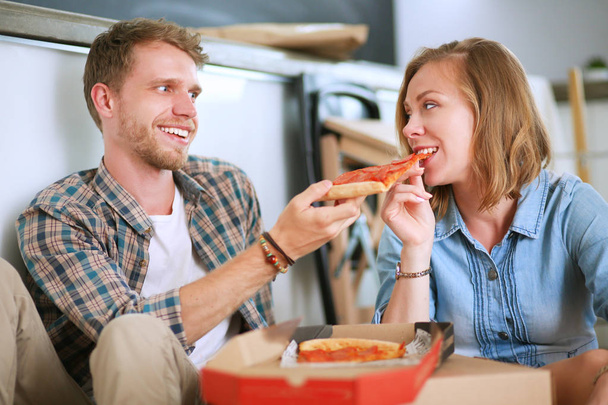 Jeune couple ont une pause déjeuner pizza sur le sol après avoir déménagé dans une nouvelle maison avec des boîtes autour d'eux
 - Photo, image