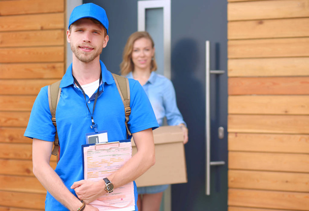 Smiling delivery man in blue uniform delivering parcel box to recipient - courier service concept - Valokuva, kuva