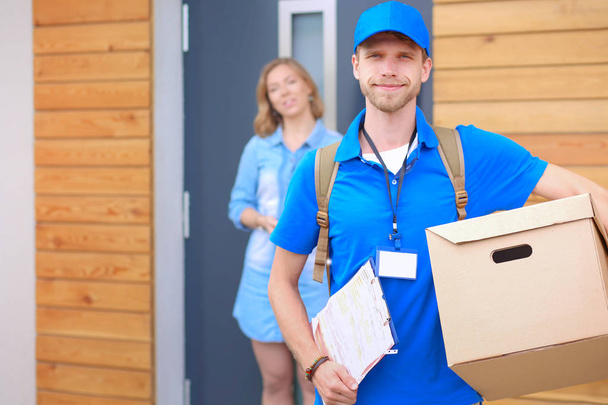 Smiling delivery man in blue uniform delivering parcel box to recipient - courier service concept - Foto, imagen