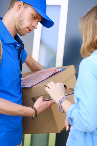 Smiling delivery man in blue uniform delivering parcel box to recipient - courier service concept - Fotó, kép