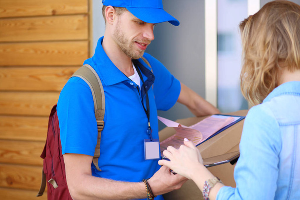 Smiling delivery man in blue uniform delivering parcel box to recipient - courier service concept - Фото, изображение