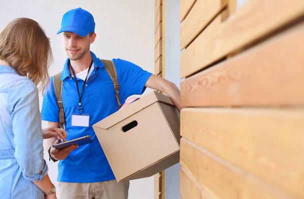Smiling delivery man in blue uniform delivering parcel box to recipient - courier service concept - Foto, Imagem