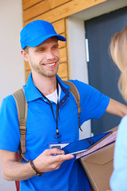 Smiling delivery man in blue uniform delivering parcel box to recipient - courier service concept - Fotoğraf, Görsel