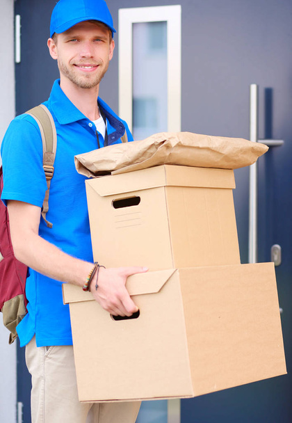 Smiling delivery man in blue uniform delivering parcel box to recipient - courier service concept - Fotó, kép