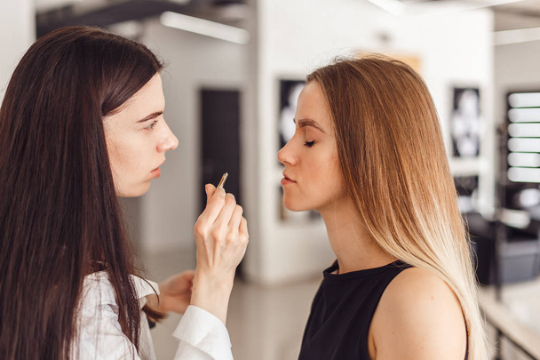 Young woman cosmetologistt weezing eyebrows of model in beauty saloon - Fotografie, Obrázek
