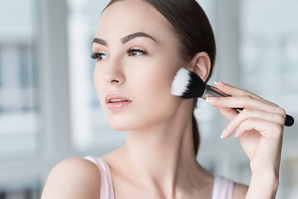 Serious attractive woman applying visage cosmetics - Фото, изображение