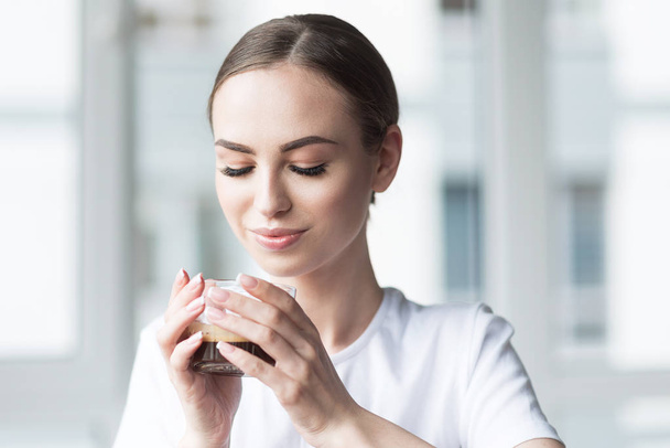 Happy young woman drinking hot beverage at home - Фото, изображение