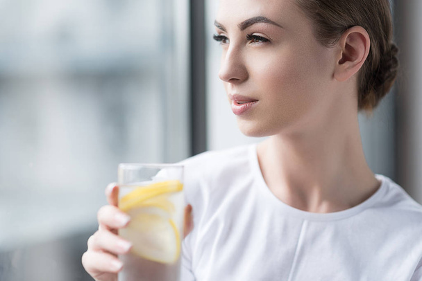 Serious beautiful girl refreshing with lemon water at home - Valokuva, kuva
