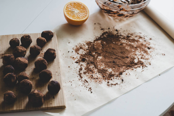A process of making healthy dessert: Chocolate truffles on the wooden board, a half of an orange and cocoa powder on the parchment paper. - Valokuva, kuva