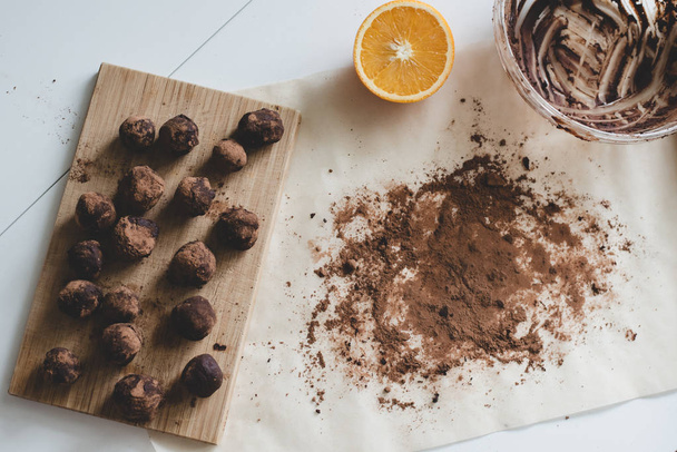 A process of making healthy dessert: Chocolate truffles on the wooden board, a half of an orange and cocoa powder on the parchment paper. - Valokuva, kuva