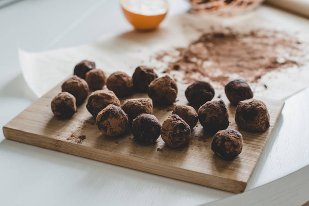 A process of making healthy dessert: Chocolate truffles on the wooden board, a half of an orange and cocoa powder on the parchment paper. - Fotoğraf, Görsel