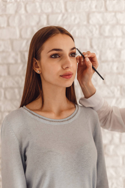 Beautiful woman and cosmetologist drawing a shape of eyebrows using cosmetic brush - Fotografie, Obrázek