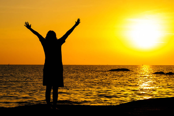 Teenager steht mit erhobenen Händen im Wasser bei Sonnenuntergang - Foto, Bild