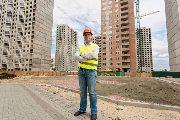Jeune travailleur en casque et gilet de sécurité debout sur le chantier
 - Photo, image