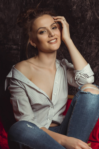 Happy brunette model with natural makeup in shirt and torn jeans - Zdjęcie, obraz