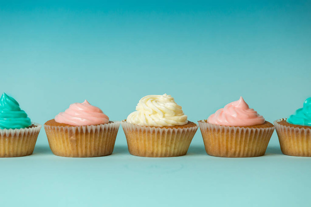 Cupcake colorati appena sfornati in fila su sfondo blu
 - Foto, immagini