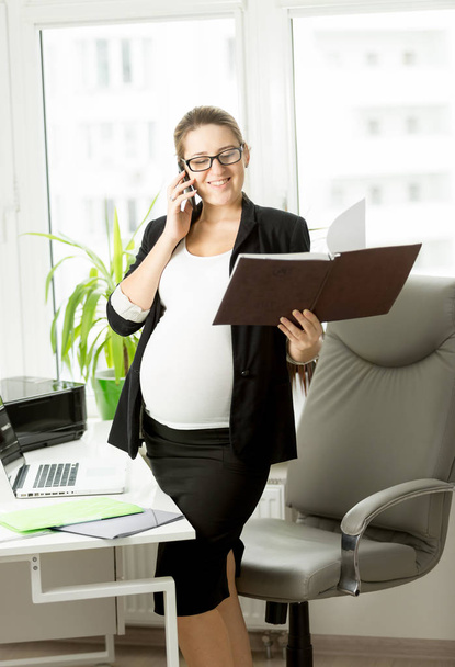 zwangere zakenvrouw in zwart pak met behulp van mobiele telefoon - Foto, afbeelding