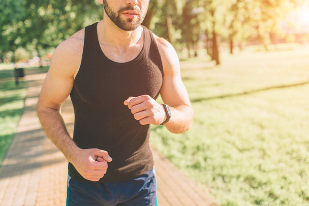 Athletic young man running in the nature. Healthy lifestyle. Bearded black haired sportsman is running on road - sunset back lit. - Foto, imagen