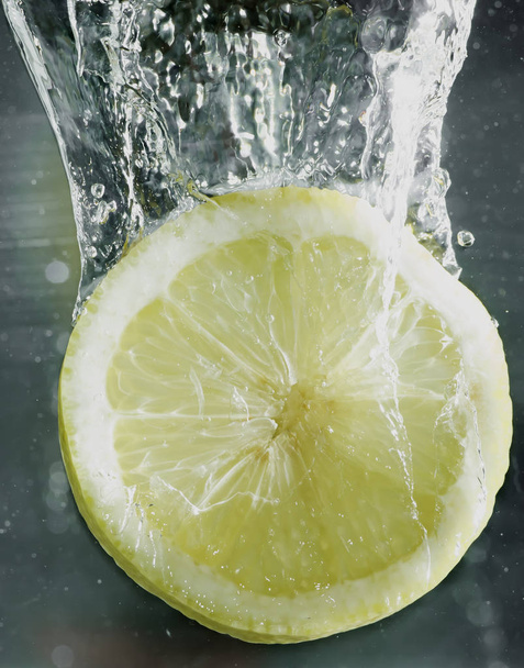 A slice of lemon drops into the water - Zdjęcie, obraz