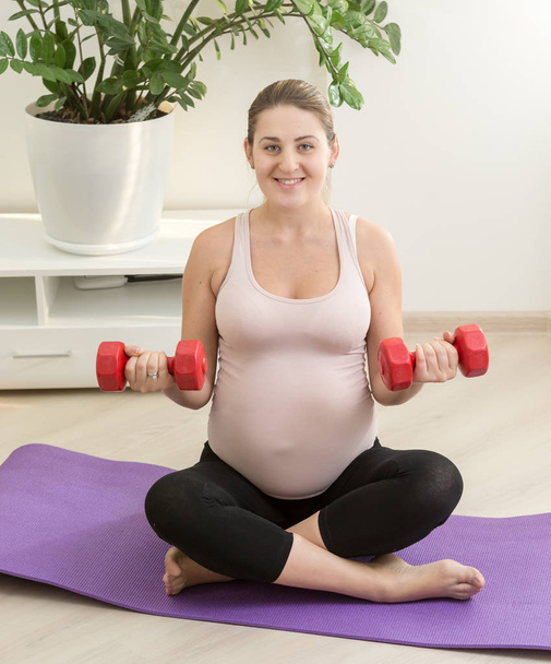 Feliz sorrindo mulher grávida se exercitando com halteres em casa
 - Foto, Imagem