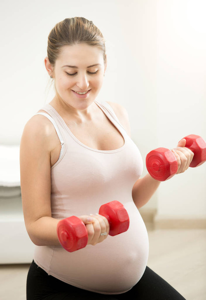 Portrait of pregnant woman sitting on mat and holding dumbbells - Foto, afbeelding