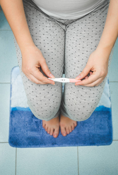 Foto de primer plano de la mujer que sostiene la prueba de embarazo positiva en bathro
 - Foto, imagen