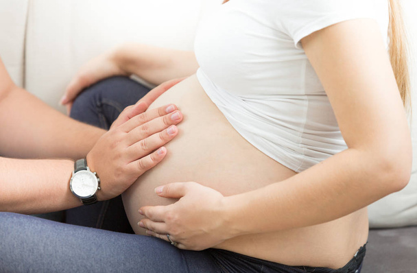 Фото крупным планом мужчины, держащегося за руки на животе беременной жены
 - Фото, изображение