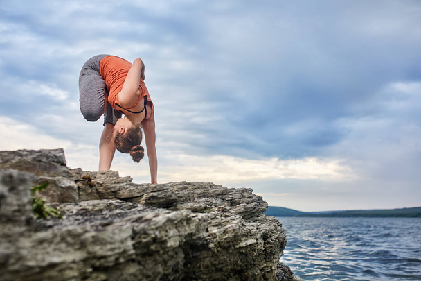Attractive woman making yoga exercise on the big stone against beautiful river. - Foto, Bild