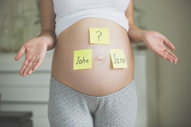 Het kiezen van de babynaam. Zwangere vrouw met namen op buik - Foto, afbeelding