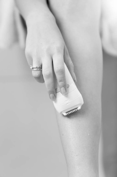Black and white closeup image of young woman holding epilator in - Photo, Image