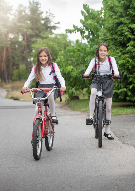 Twee mooie lachende schoolmeisjes rijden naar school op de fiets - Foto, afbeelding