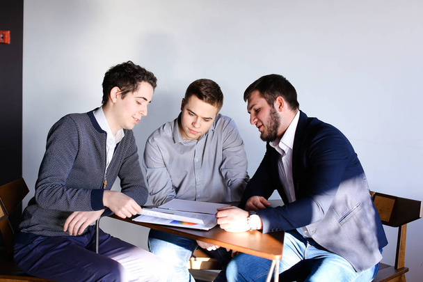 Três jovens programadores do sexo masculino se comunicam usando tablet enquanto sentam
 - Foto, Imagem