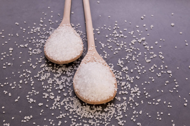 Coarse salt in wooden spoons on a black background - Photo, Image
