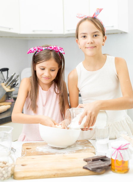 Two sisters making dough on kitchen in big white bowl - Zdjęcie, obraz